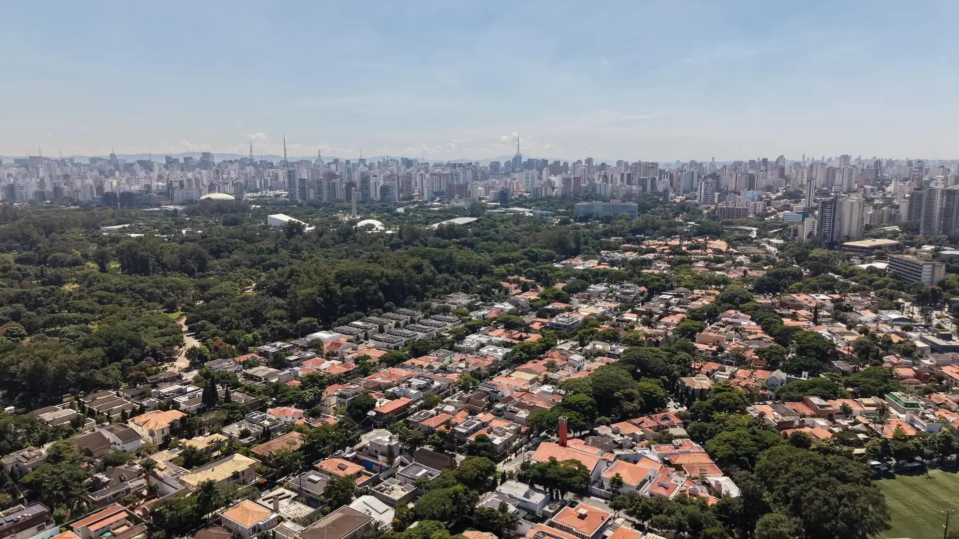 Bairro arborizado ao lado do Parque Ibirapuera e a cidade no horizonte. Foto aérea.
